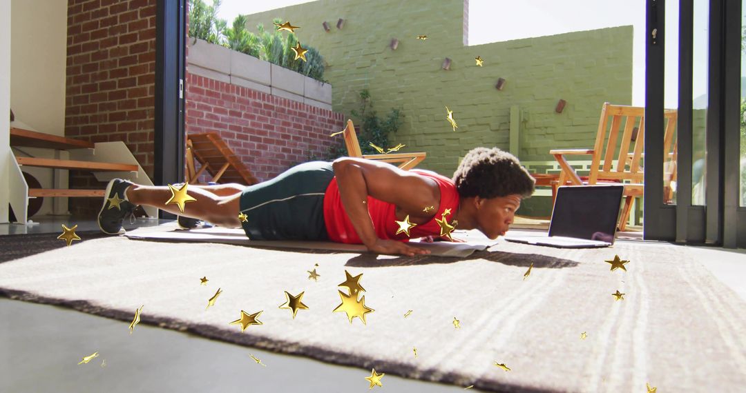Man following online workout doing push-up on rug by open patio doors