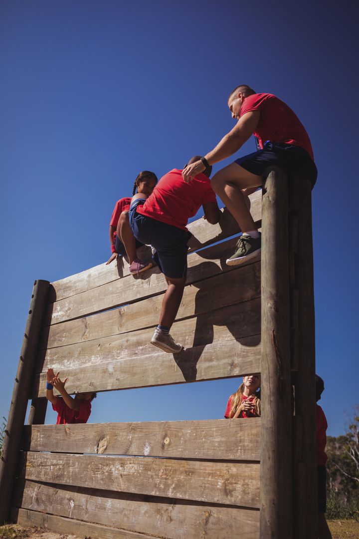 Trainer assisting kids to climb a wooden wall during obstacle course training - Free Images, Stock Photos and Pictures on Pikwizard.com