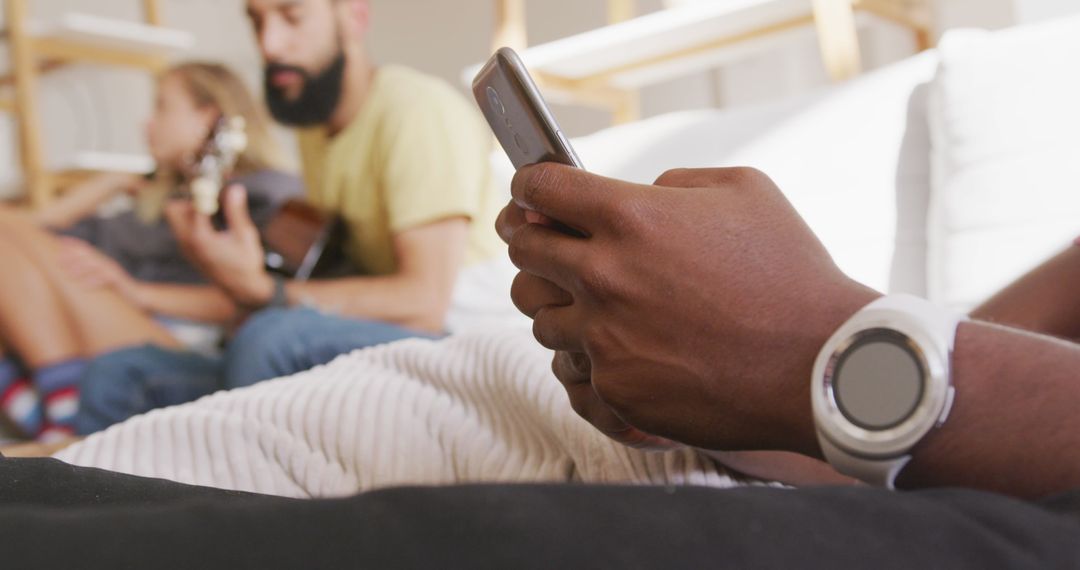 Man Relaxing with Smartphone While Friends Play Music in Background