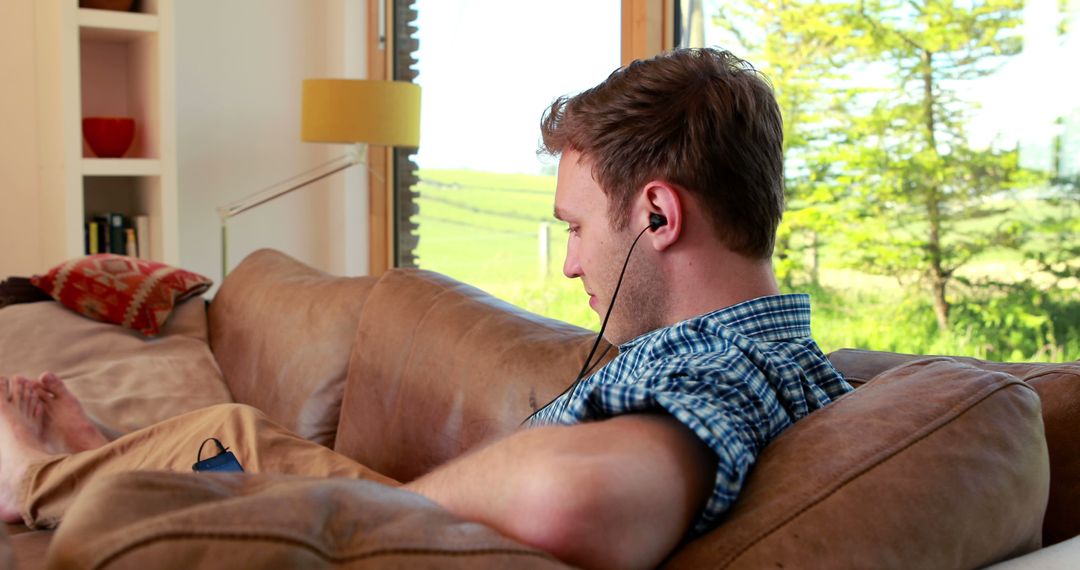 Young Adult Enjoying Music on Couch by Sunny Window - Free Images, Stock Photos and Pictures on Pikwizard.com