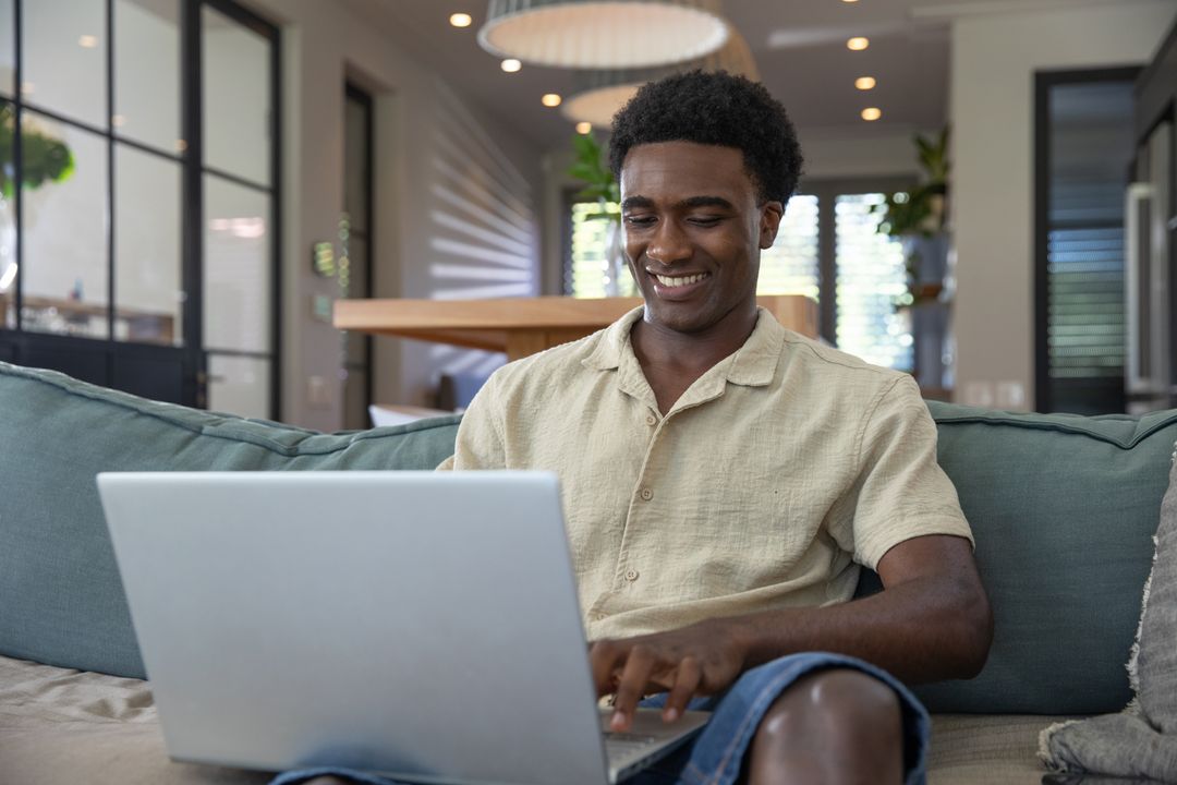 Smiling Man Using Laptop on Sofa at Home