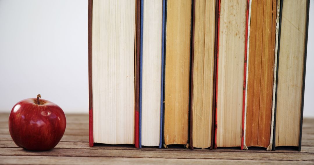 A red apple sits next to a row of upright books on a wooden surface, with copy space - Free Images, Stock Photos and Pictures on Pikwizard.com