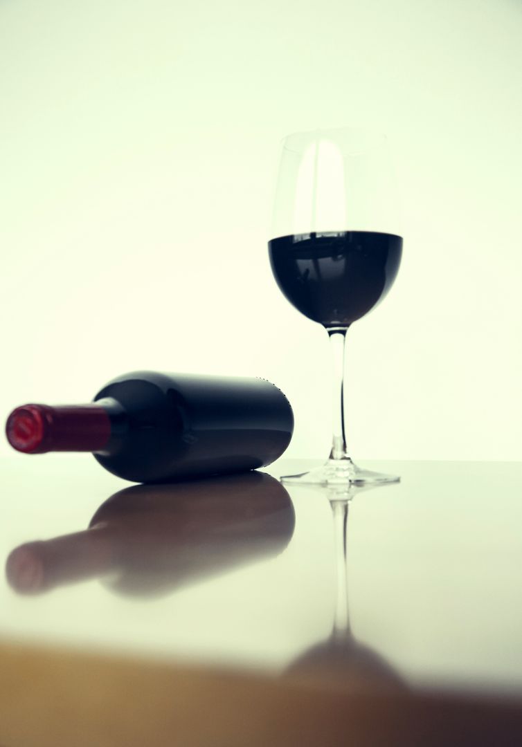 Minimalist red wine bottle lying with glass reflecting on glossy surface