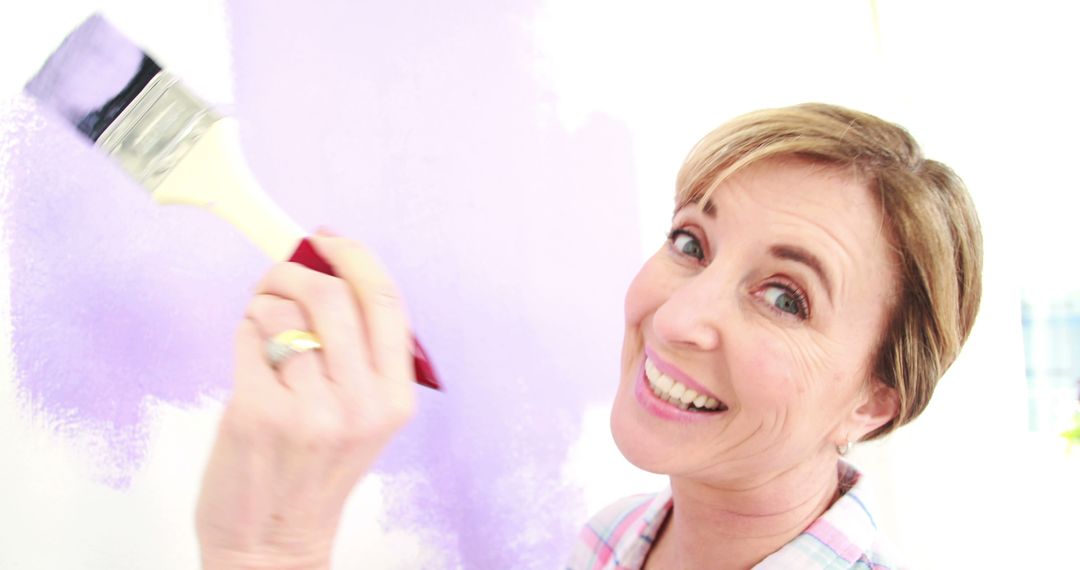 Smiling Woman Painting Wall with Purple Paint Brush - Free Images, Stock Photos and Pictures on Pikwizard.com