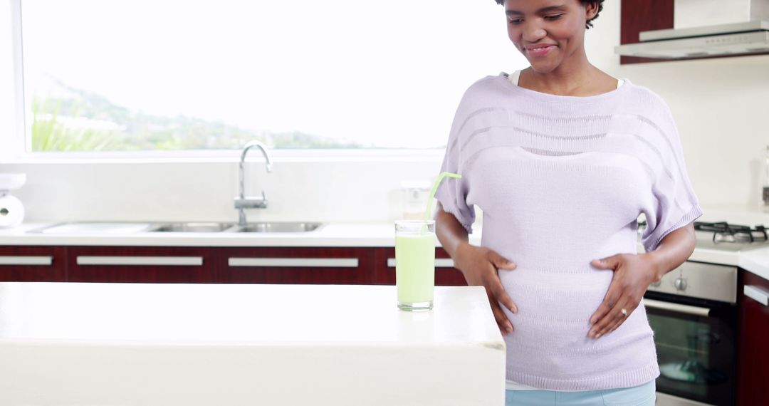 Pregnant woman standing in modern kitchen with green smoothie - Free Images, Stock Photos and Pictures on Pikwizard.com