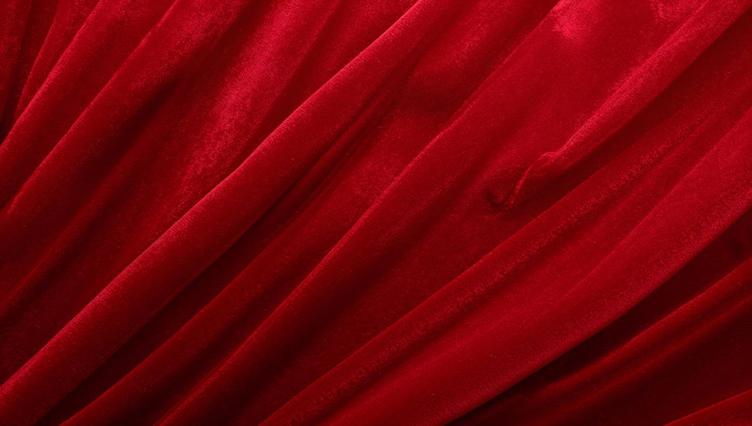 Crimson velvet fabric forming diagonal folds with rich nap, sheen and plush texture