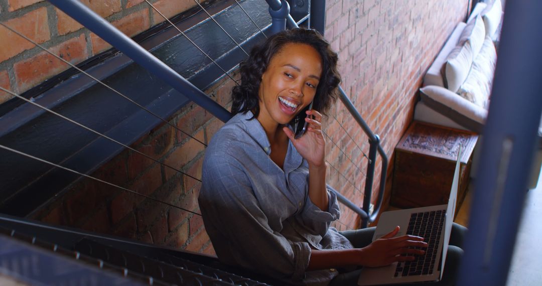 Smiling Young Woman Talking on Phone and Using Laptop - Free Images, Stock Photos and Pictures on Pikwizard.com