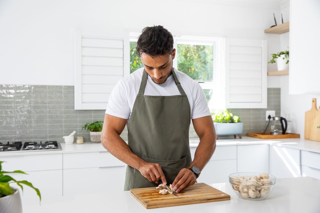 Man in Apron Slicing Fresh Mushrooms in Modern Kitchen