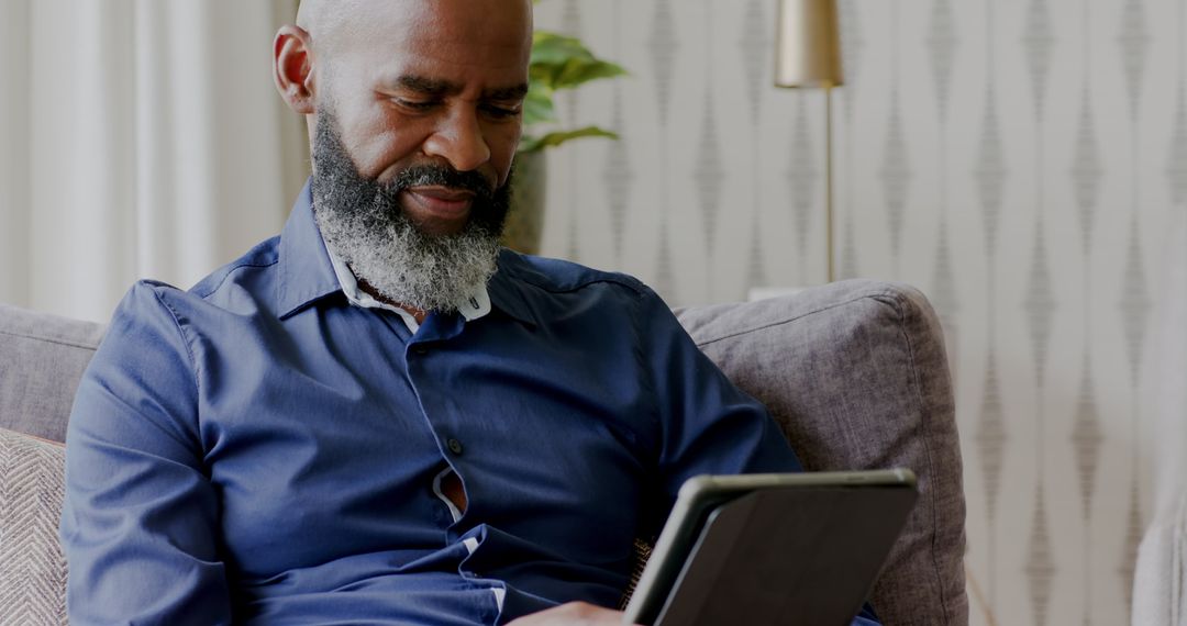 Mature Man Engaged in Tablet Use on Comfortable Sofa