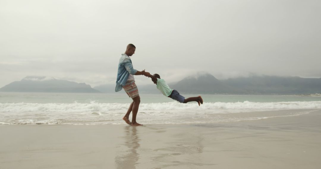 Father Spinning Son on Beach with Ocean View - Free Images, Stock Photos and Pictures on Pikwizard.com