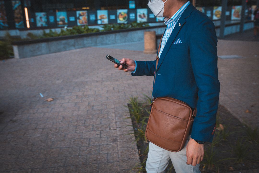 Mid section of asian man wearing face mask using smartphone while walking at at corporate park - Free Images, Stock Photos and Pictures on Pikwizard.com