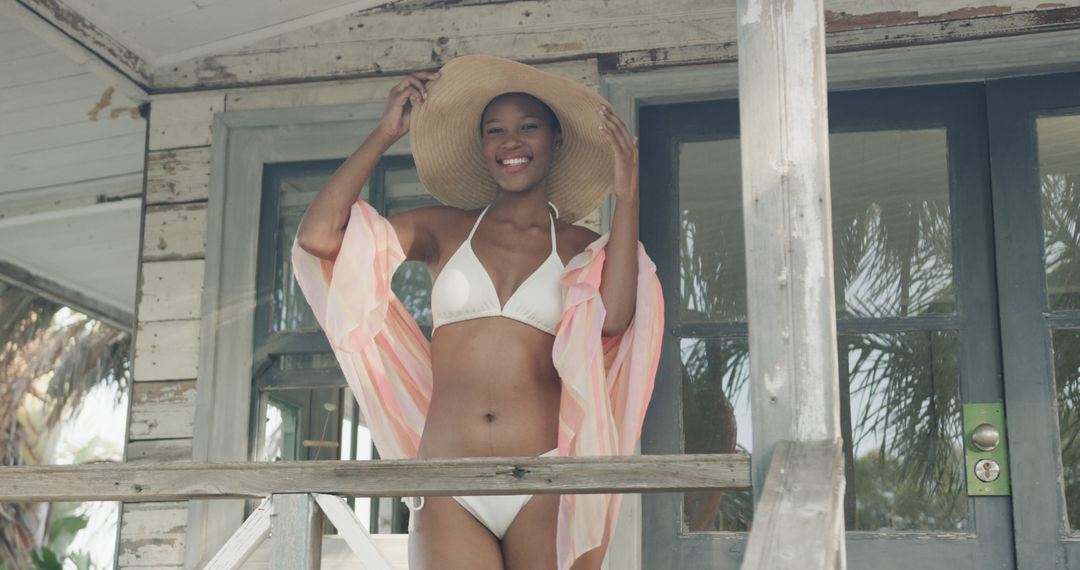 Portrait of biracial woman in bikini and sunhat smiling on porch of wooden beach house, slow motion - Free Images, Stock Photos and Pictures on Pikwizard.com