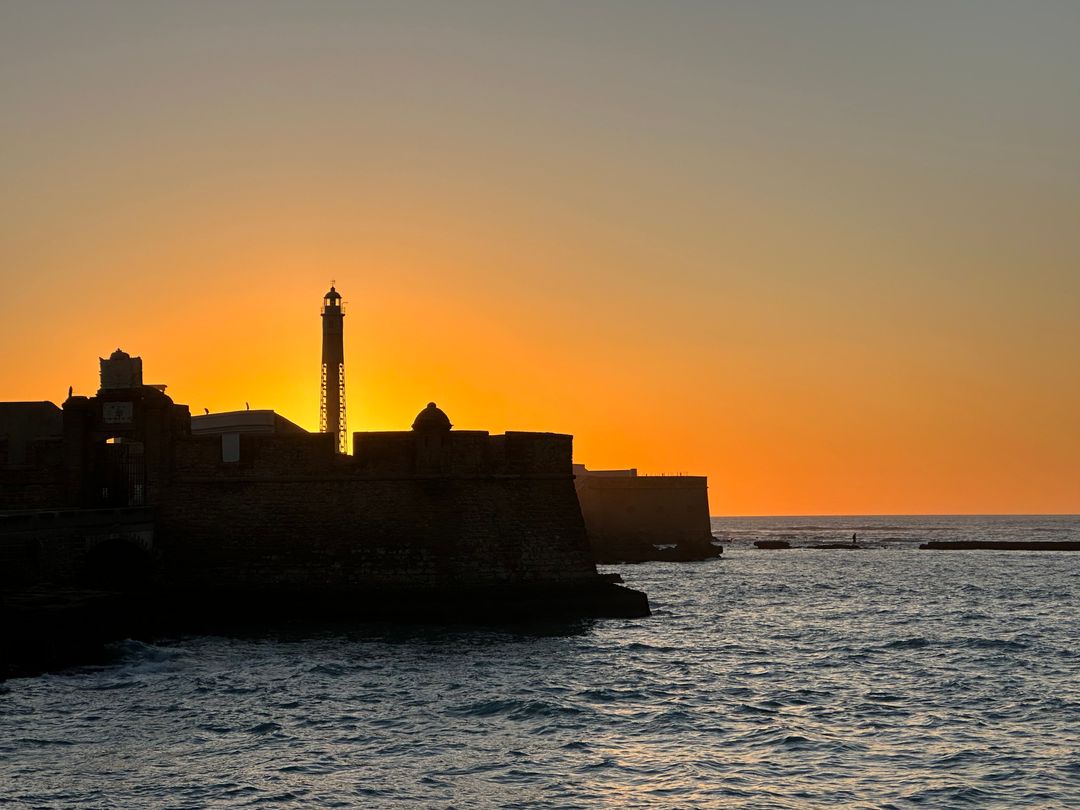 Sunset Silhouettes over Coastal Fortress with Lighthouse Beacon