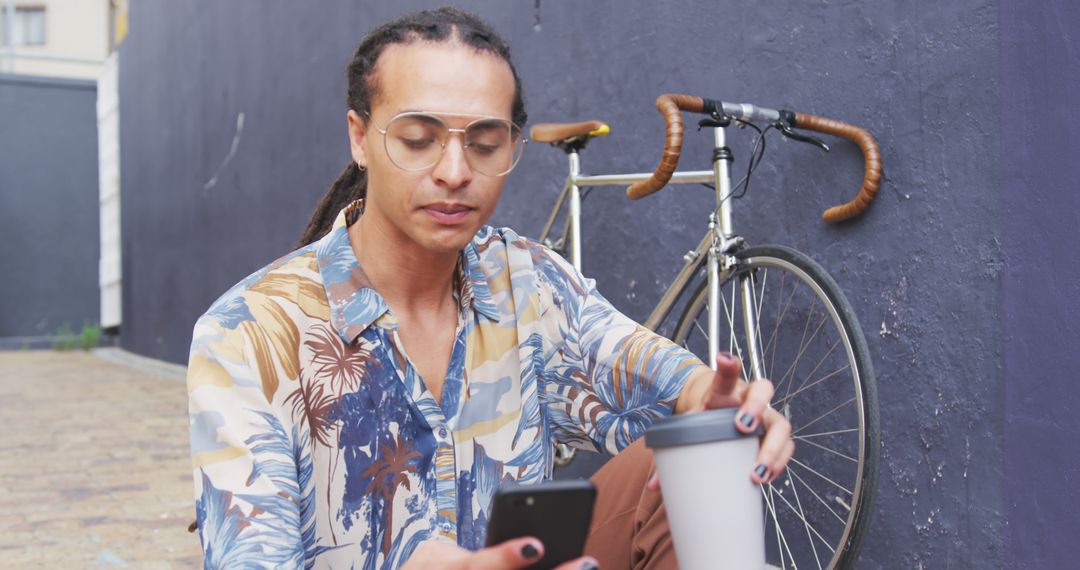 A biracial man with dreadlocks enjoys coffee and his smartphone by his bike in the city. - Free Images, Stock Photos and Pictures on Pikwizard.com