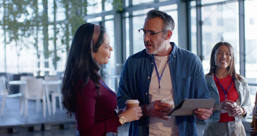 Diverse team networking in modern glass atrium holding coffee and tablet