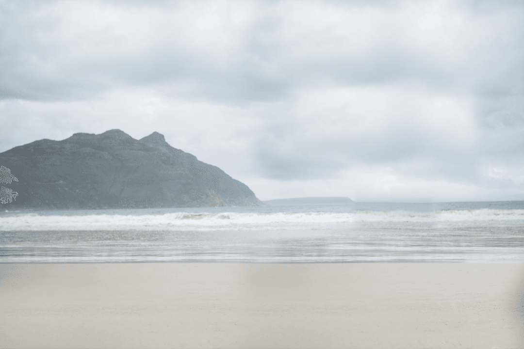 Transparent Tranquil Beach with Mountain View Under Cloudy Sky