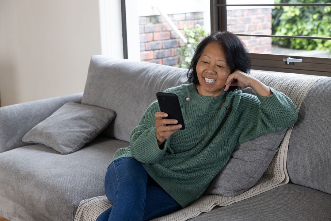 Senior Asian Woman Relaxing on Sofa Using Smartphone