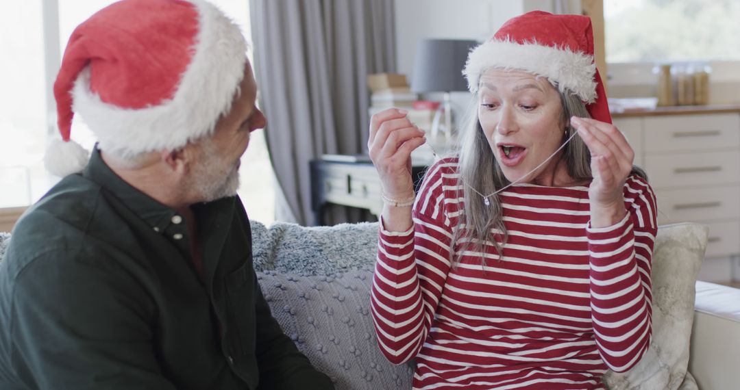 Excited Senior Couple Exchanging Christmas Gifts in Santa Hats - Free Images, Stock Photos and Pictures on Pikwizard.com