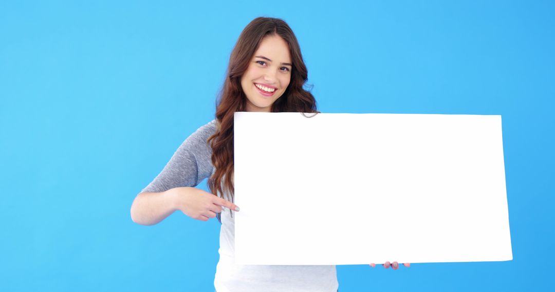 Smiling Young Woman Holding and Pointing at Blank Sign - Free Images, Stock Photos and Pictures on Pikwizard.com