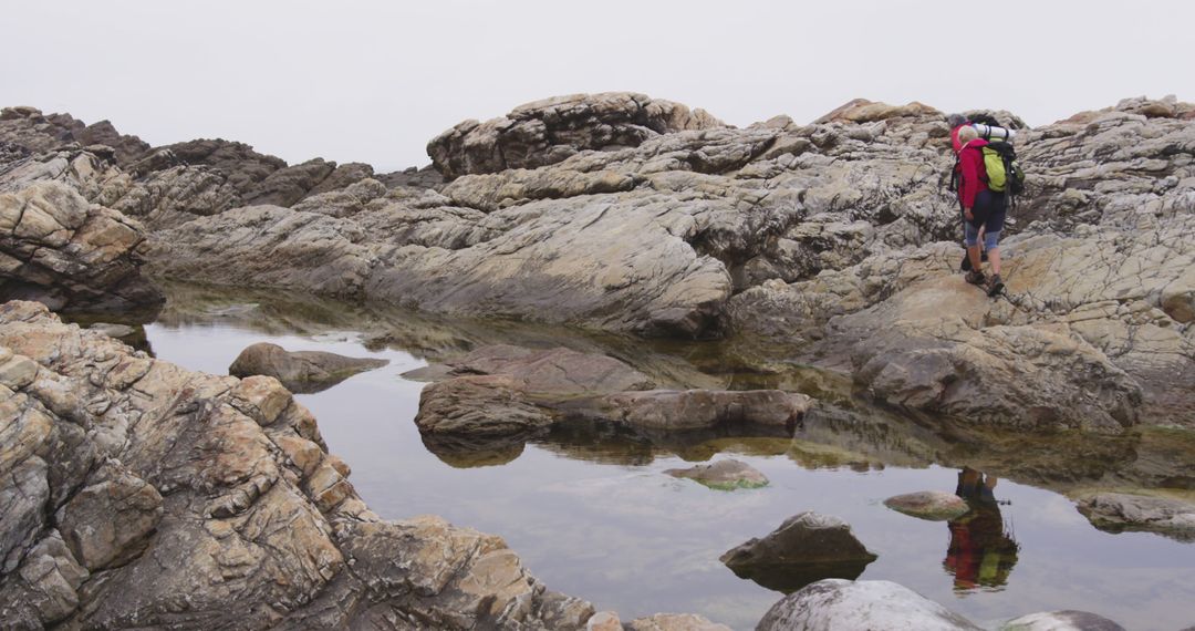 Hiker Climbing Rocky Terrain Near Reflective Water Pools - Free Images, Stock Photos and Pictures on Pikwizard.com