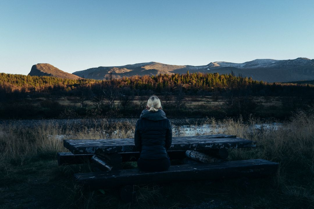 Woman Sitting on Bench Facing Serene Mountain Landscape at Sunset - Free Images, Stock Photos and Pictures on Pikwizard.com