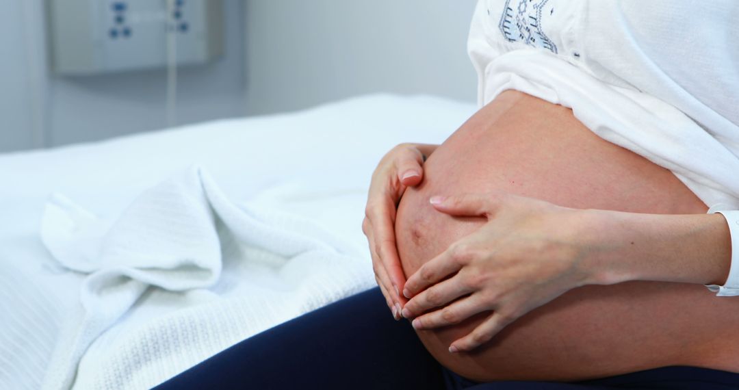 Expectant Mother Cradling Belly in Prenatal Clinic Environment - Free Images, Stock Photos and Pictures on Pikwizard.com