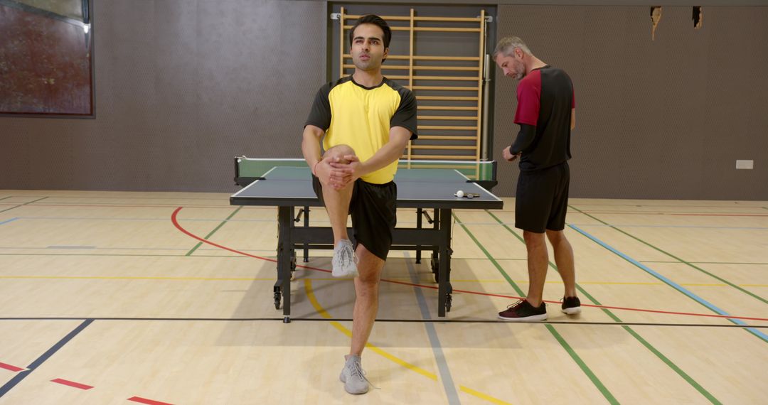Teammates Stretching in Gym with Table Tennis Setup