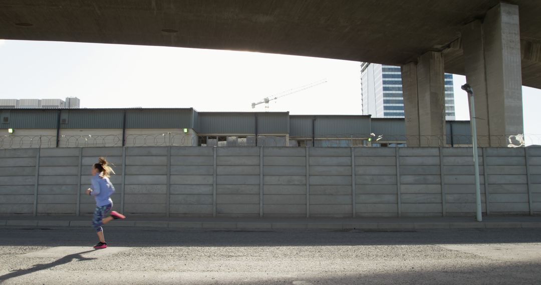 Woman Jogging Under Urban Overpass with Modern Buildings - Free Images, Stock Photos and Pictures on Pikwizard.com