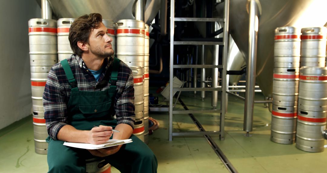 Brewery Worker Taking Notes Surrounded by Metal Beer Kegs - Free Images, Stock Photos and Pictures on Pikwizard.com