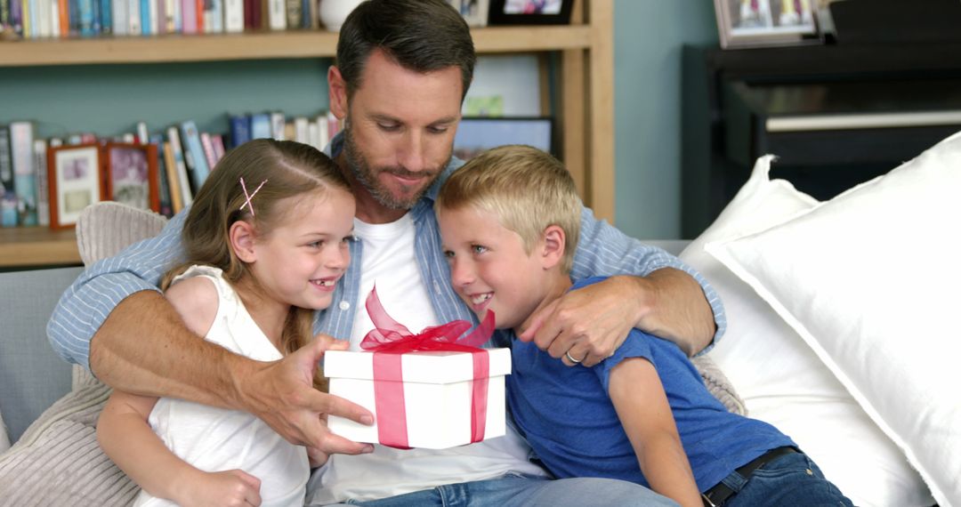 Father and Children Sharing a Gift While Sitting on Couch - Free Images, Stock Photos and Pictures on Pikwizard.com