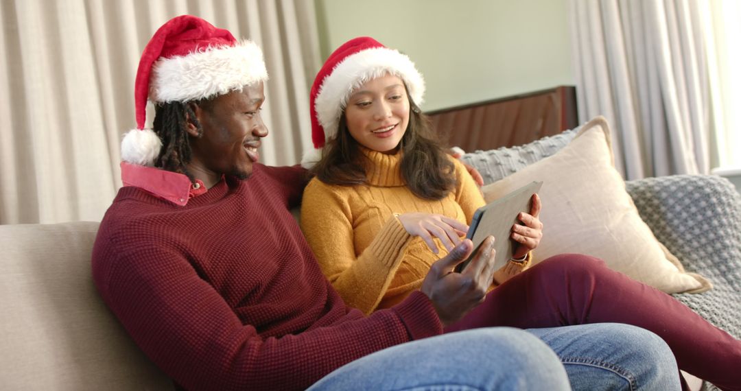 Happy Couple in Santa Hats Using Tablet at Home During Christmas Season - Free Images, Stock Photos and Pictures on Pikwizard.com