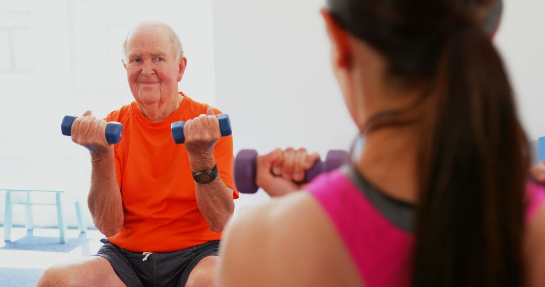 Senior Man Exercising with Female Trainer Using Dumbbells in Studio