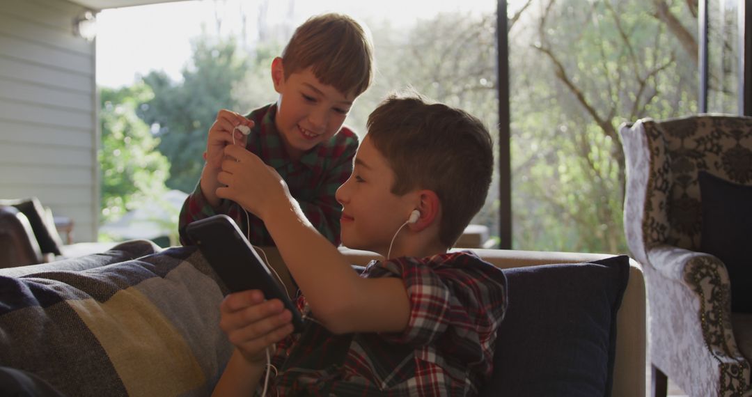 Young Boys Sharing Earphones and Music on Smartphone at Home - Free Images, Stock Photos and Pictures on Pikwizard.com