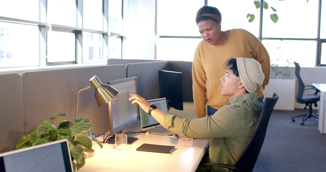 Diverse coworkers collaborating in modern open-plan office, team member pointing at monitor