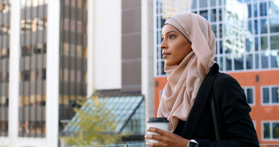 Confident Businesswoman Wearing Hijab Holding Coffee Cup in Modern Urban Area - Free Images, Stock Photos and Pictures on Pikwizard.com