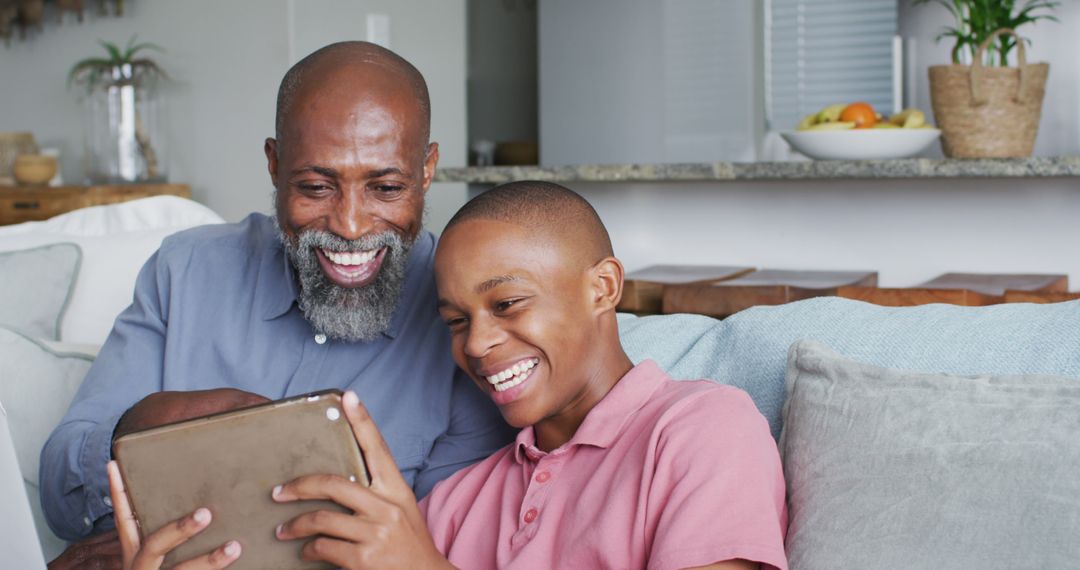 Happy African American Father and Son Watching Tablet on Couch - Free Images, Stock Photos and Pictures on Pikwizard.com