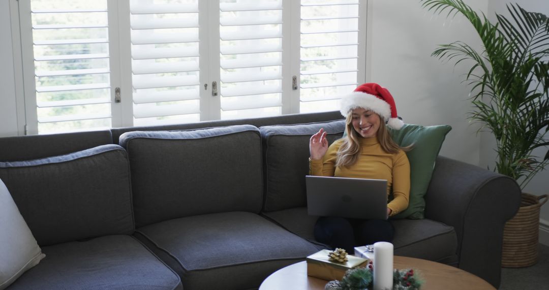 Woman Wearing Santa Hat Video Chatting on Laptop During The Holidays on a Gray Sofa - Free Images, Stock Photos and Pictures on Pikwizard.com