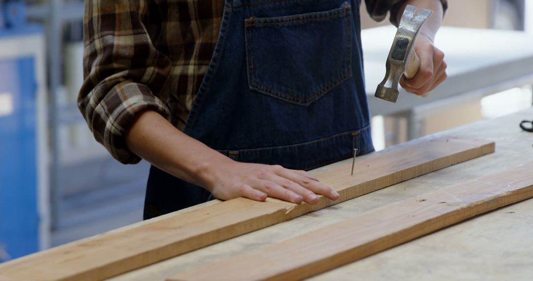 Carpenter Wearing Denim Apron Hammering Nail in Workshop - Free Images, Stock Photos and Pictures on Pikwizard.com