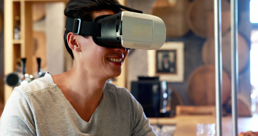 Young Man Smiling Wearing Virtual Reality Headset in Modern Cafe - Free Images, Stock Photos and Pictures on Pikwizard.com