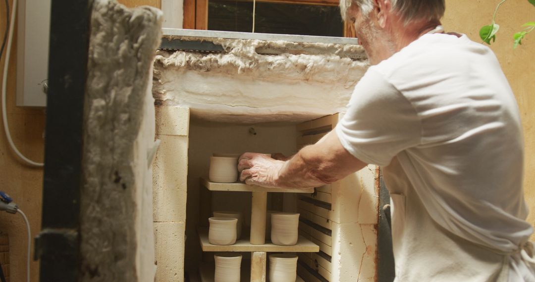 Senior Artisan Firing Pottery in Kiln at Workshop