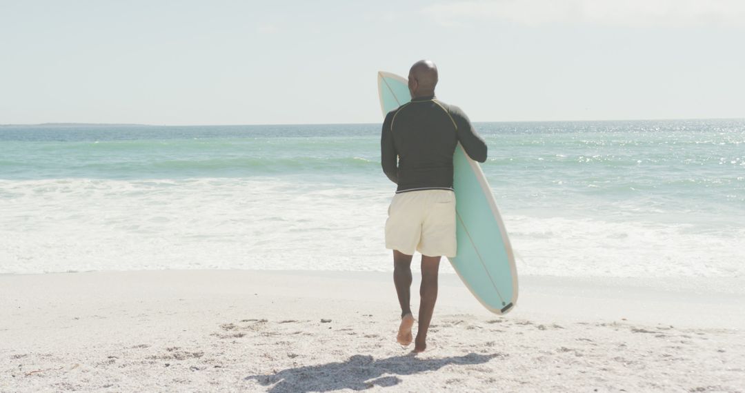 Man Walking on Beach Carrying Surfboard Towards Ocean - Free Images, Stock Photos and Pictures on Pikwizard.com