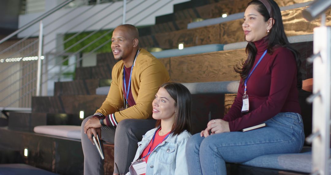 Diverse colleagues attending seminar on tiered benches wearing lanyards holding tablet and notebook