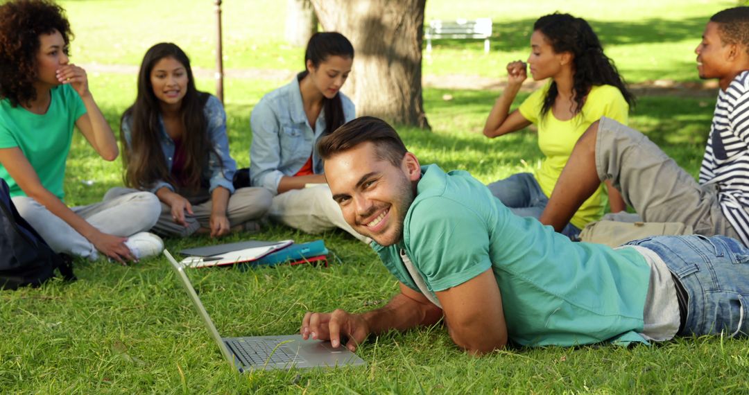 Young Man Studying on Laptop Outdoors with Friends on Sunny Day - Free Images, Stock Photos and Pictures on Pikwizard.com