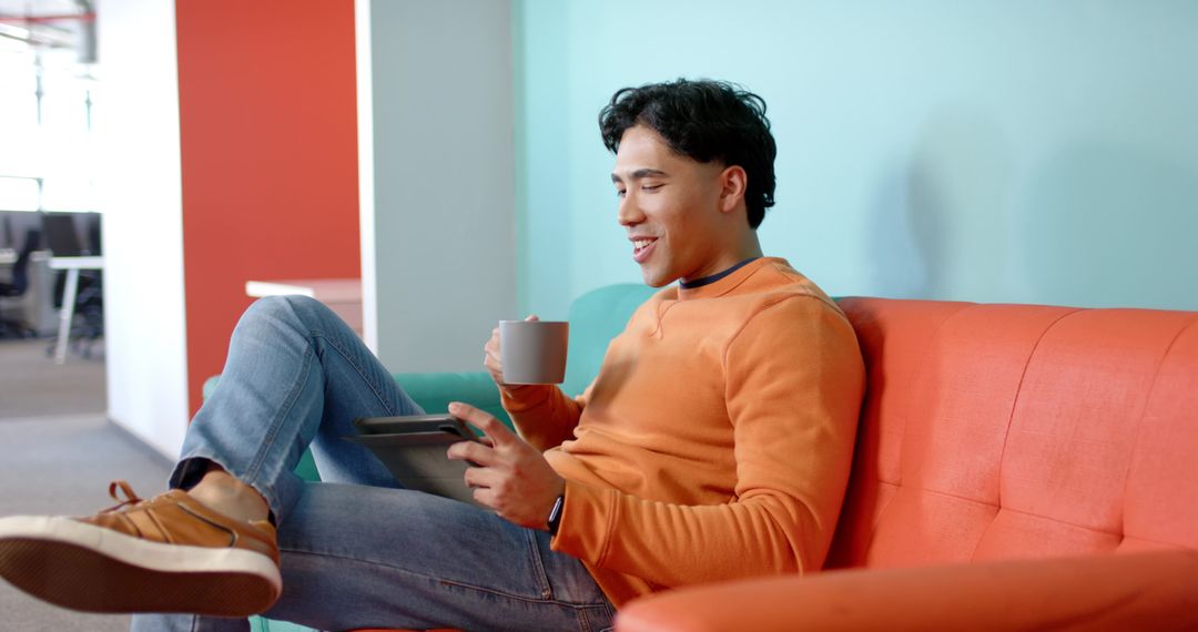 Young Man Relaxing on Sofa in Coworking Lounge with Tablet and Coffee