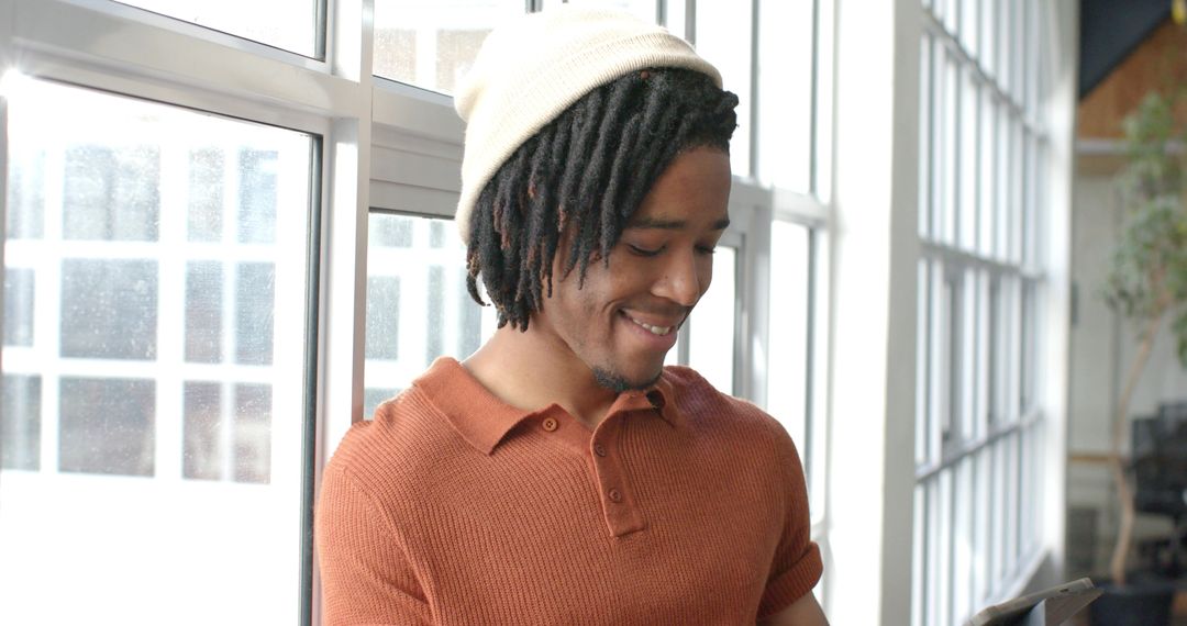 African American Man Leaning by Window Checking Tablet in Bright Coworking Workspace