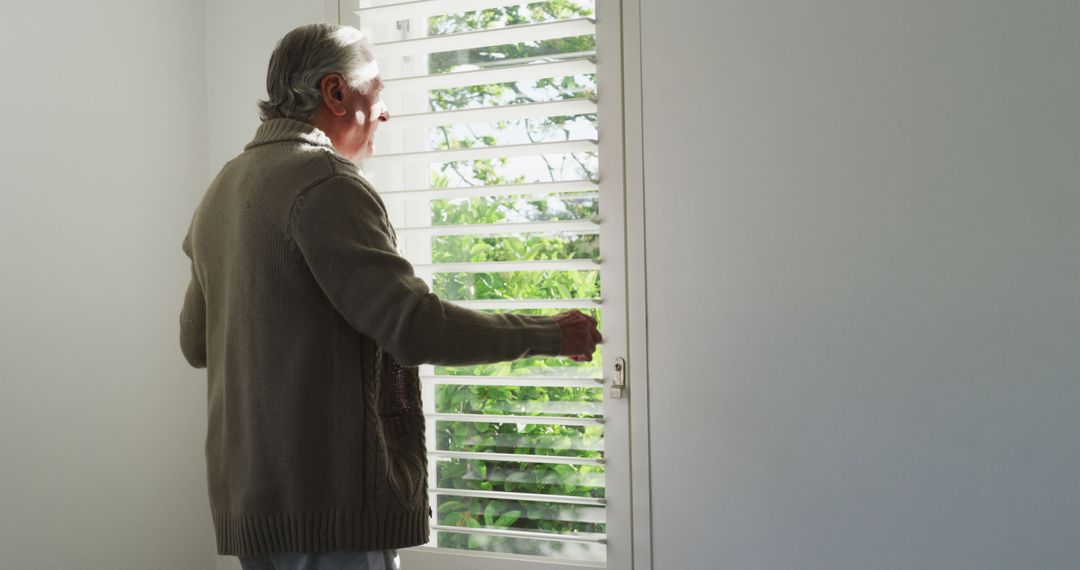 Elderly Man Looking Through Window Blinds in Sunlit Room - Free Images, Stock Photos and Pictures on Pikwizard.com