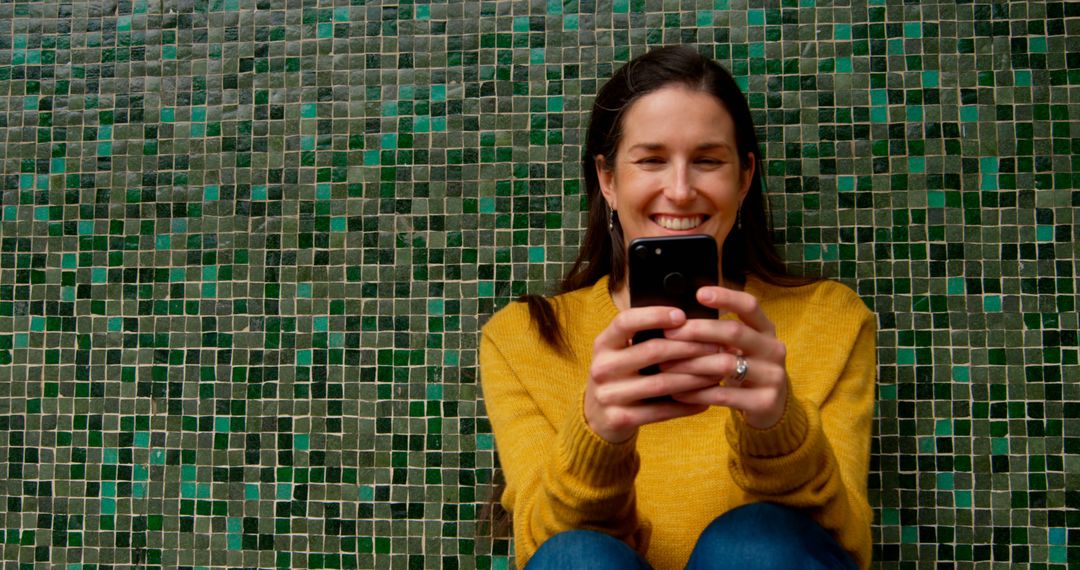 Happy Woman using Smartphone in Front of Green Mosaic Wall - Free Images, Stock Photos and Pictures on Pikwizard.com