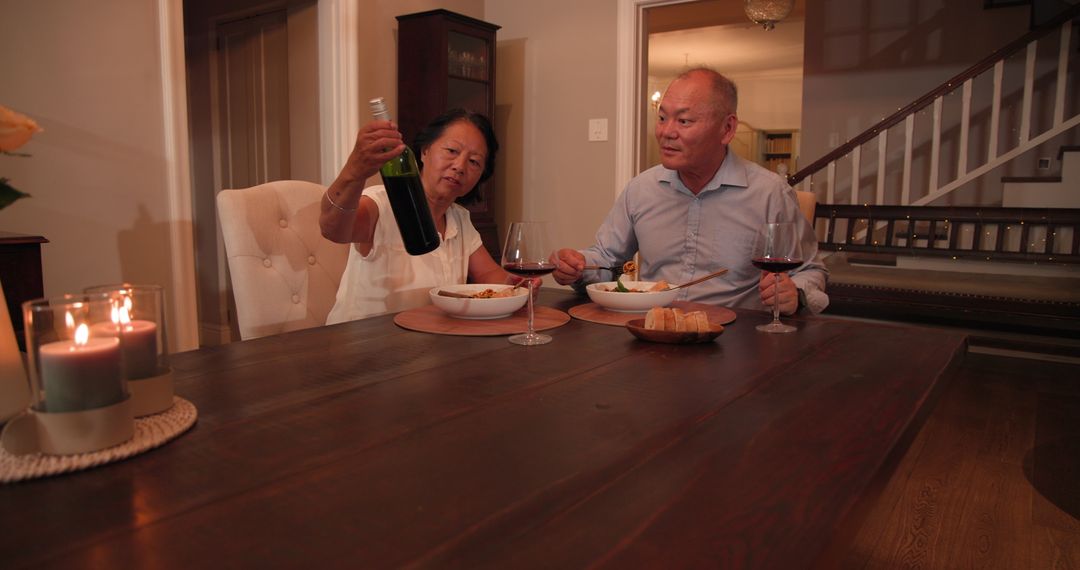 Senior Asian Couple Enjoying Dinner at Home with Wine and Conversation