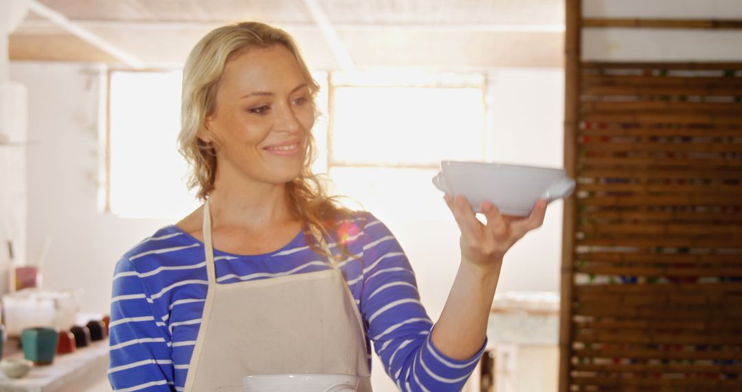 Woman Wearing Apron Smiling Holding Ceramic Bowl in Studio - Free Images, Stock Photos and Pictures on Pikwizard.com