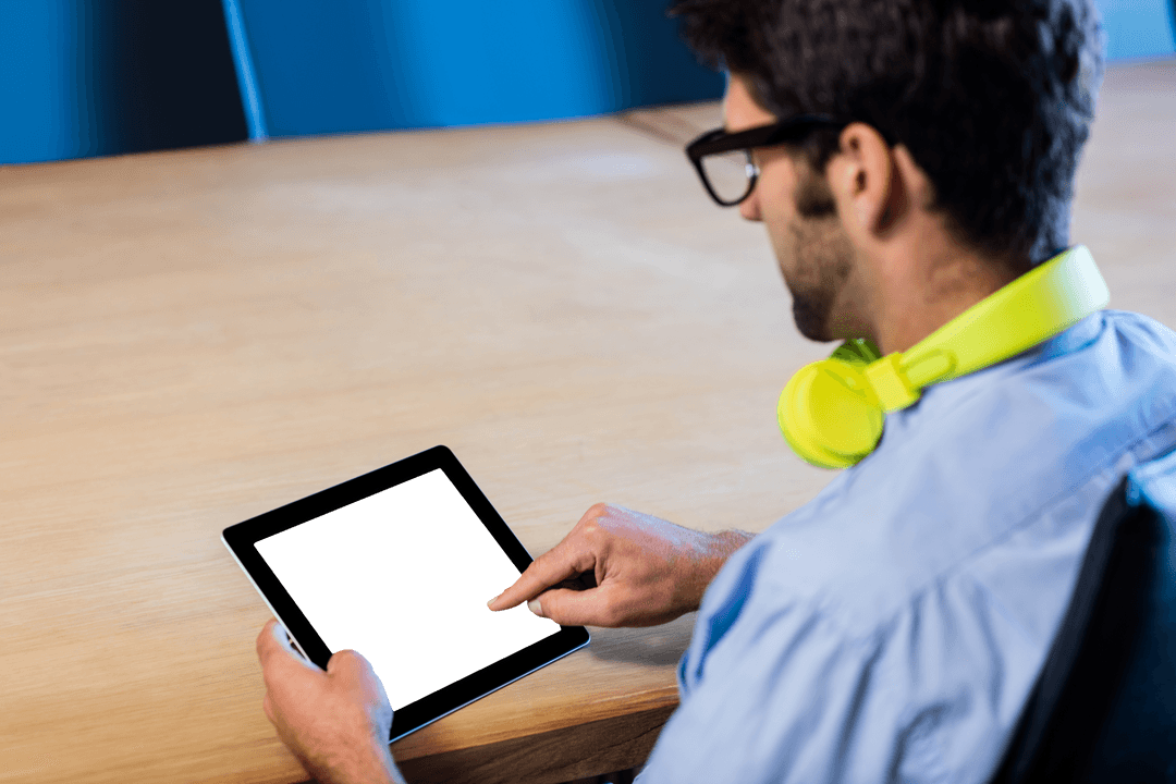 Man Wearing Headphones Using Transparent Digital Tablet at Work Desk
